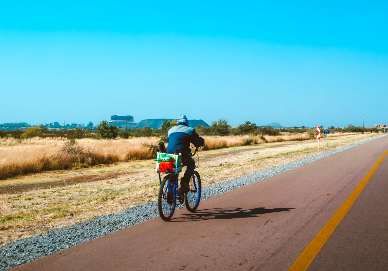 about-img A lone cyclist travels on an open rural road in sunny South Africa, enjoying a peaceful adventure.